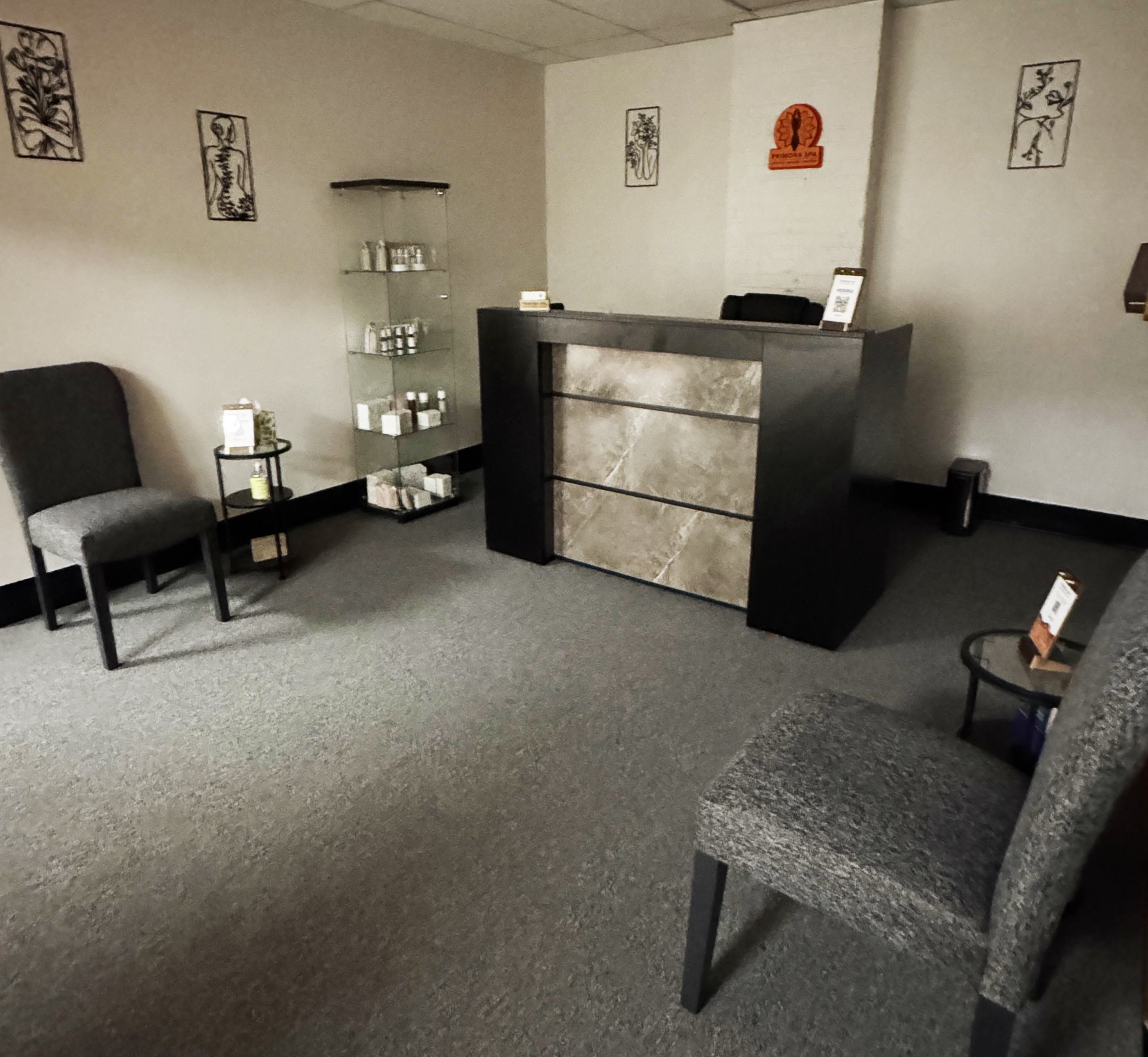 Reception area with a dark marble counter, gray chairs, and a glass display shelf of products against beige walls.