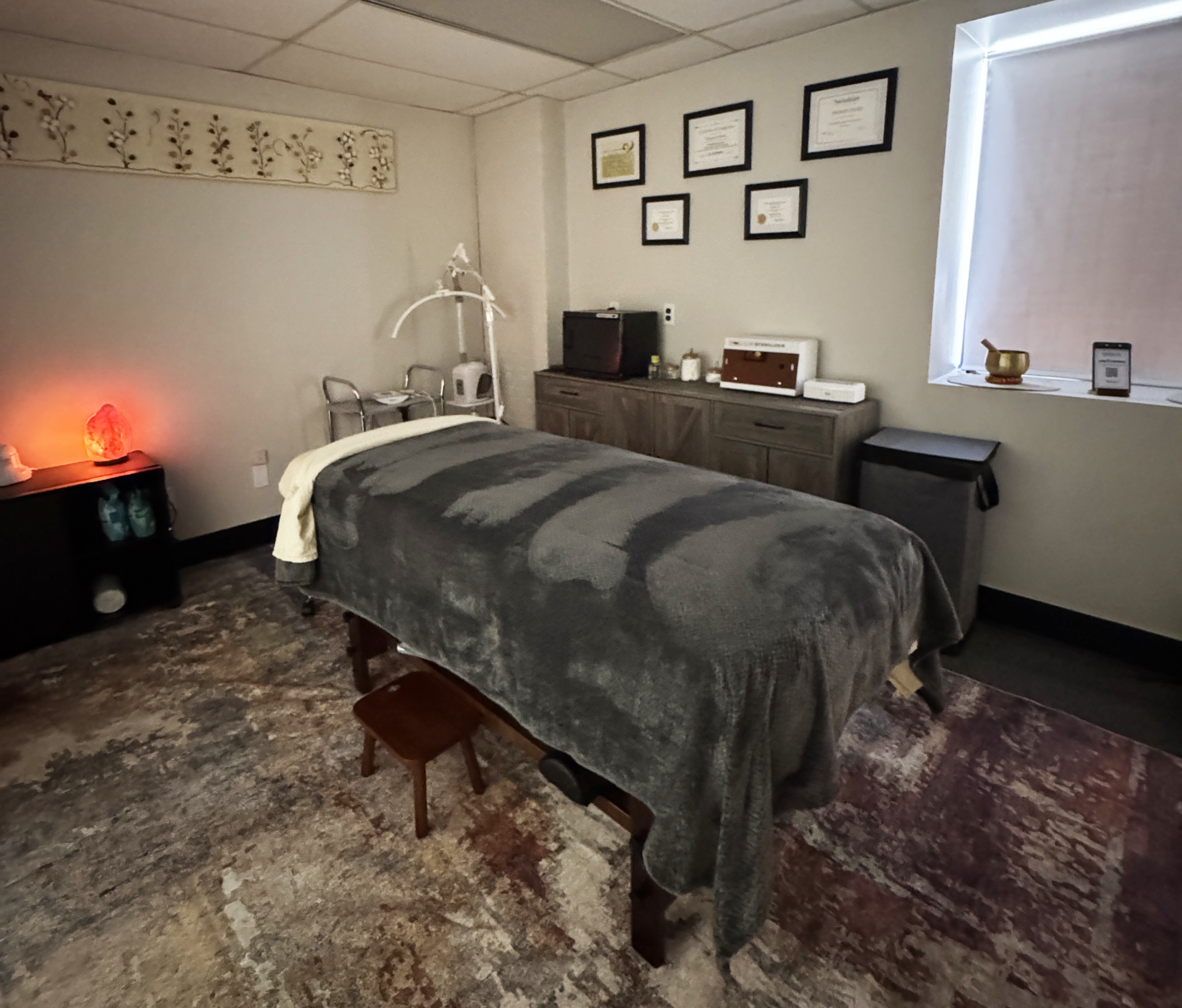 Treatment room with a massage bed covered in a gray blanket, and a small stool nearby